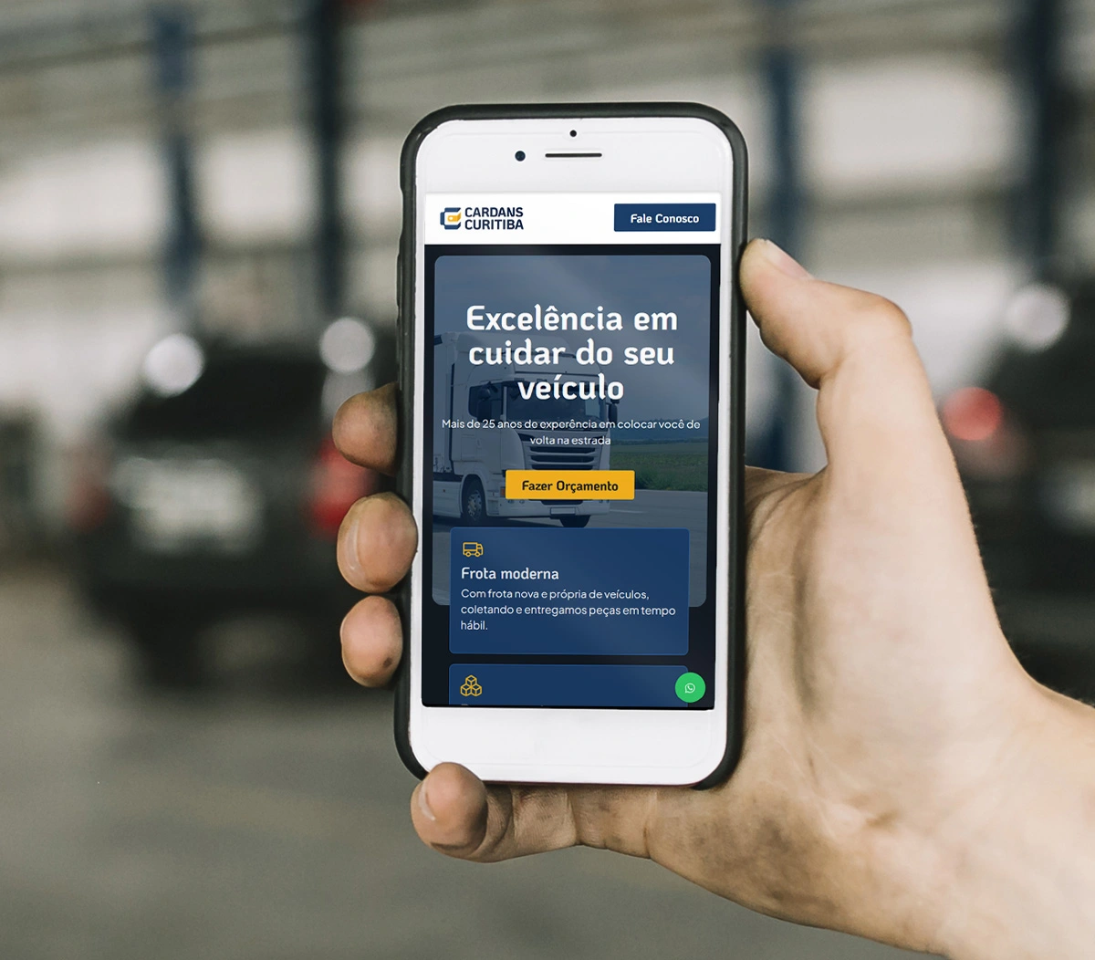 A hand holding a smartphone displaying a portion of the homepage